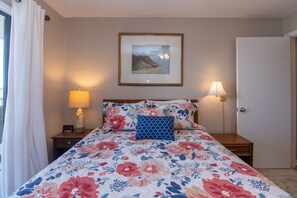 Una camera da letto con una coperta a fiori, un quadro appeso al muro, lampade sui comodini e un comodino con una sveglia.