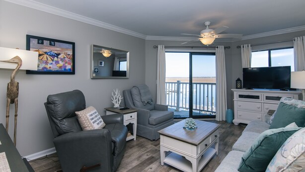 A living room with a gray leather sofa, a white coffee table, and a gray armchair. There is a large window with a view of the ocean. - 216 Bay Creek Villa-Beautiful 2nd Floor Villa;Private Balcony;Water Views;Communal Pool (Edisto Beach)