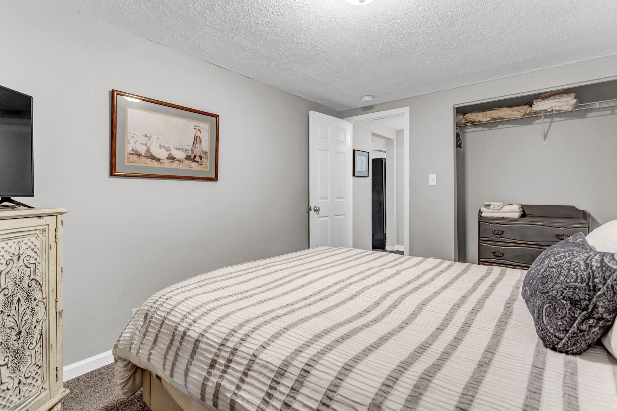 A bedroom with a bed, dresser, and a painting on the wall.