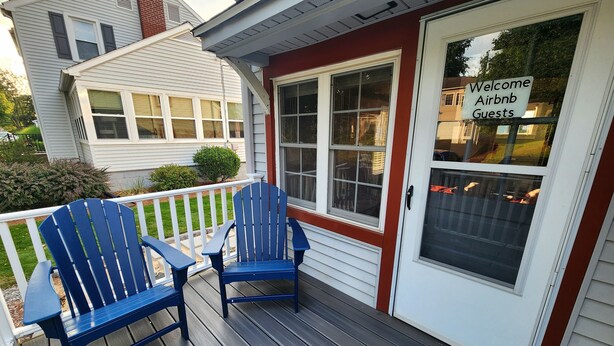 Un porche con dos sillas Adirondack azules y un letrero en la puerta que dice 'Welcome Airbnb Guests'.