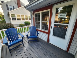 Un porche con dos sillas Adirondack azules y un letrero en la puerta que dice 'Welcome Airbnb Guests'.