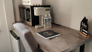 Una kitchenette compacta con microondas, cafetera y botellas de agua sobre una mesa de madera.
