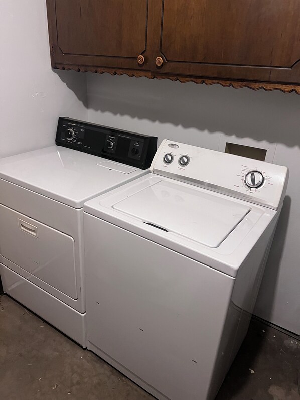 Una lavadora y secadora de carga frontal, con paneles de control, ubicada en un cuarto de lavado con armarios de madera arriba.