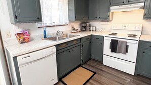 A kitchen with grey cabinets, a white dishwasher, a stove, and a coffee maker. - COZY 2Bedroom/1Bath Duplex  (Enid)