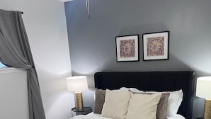 A neatly made bed with a dark headboard, two bedside lamps, and a decorative wall hanging. - COZY 2Bedroom/1Bath Duplex  (Enid)