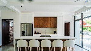A modern kitchen with a central island, bar stools, a refrigerator, and wooden cabinets. - Elegant Modern Villa with Private Pool & Rooftop, Near Beach and City Center (Tamarindo)