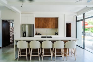 A modern kitchen with a central island, bar stools, a refrigerator, and wooden cabinets. - Elegant Modern Villa with Private Pool & Rooftop, Near Beach and City Center (Tamarindo)