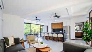 A modern living room with a sofa, coffee table, and chairs. A kitchen is visible in the background with a bar area. - Elegant Modern Villa with Private Pool & Rooftop, Near Beach and City Center (Tamarindo)