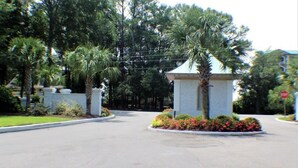 A gated entrance with a small kiosk, palm trees, and a stop sign in the background. - Rhue's Haven less than 5 minutes from the most wonderful beach in NC (Sunset Beach)