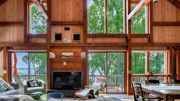 A spacious cabin with a large TV in the center, wooden walls, and large windows offering views of the surrounding forest.