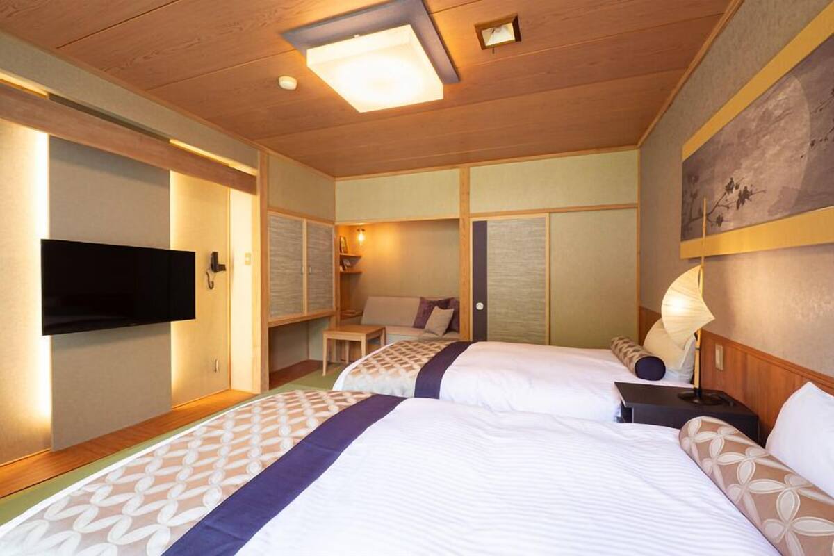 A hotel room with two beds, a flat-screen TV, a desk, and a lamp.