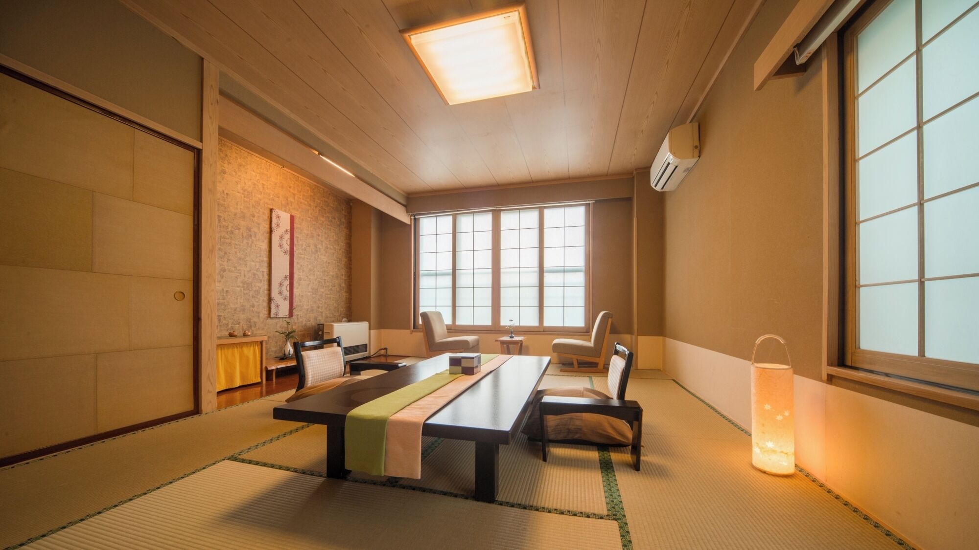 Una habitación japonesa tradicional con suelo de tatami, una mesa baja, sillas, un celosía de papel y una puerta corredera.