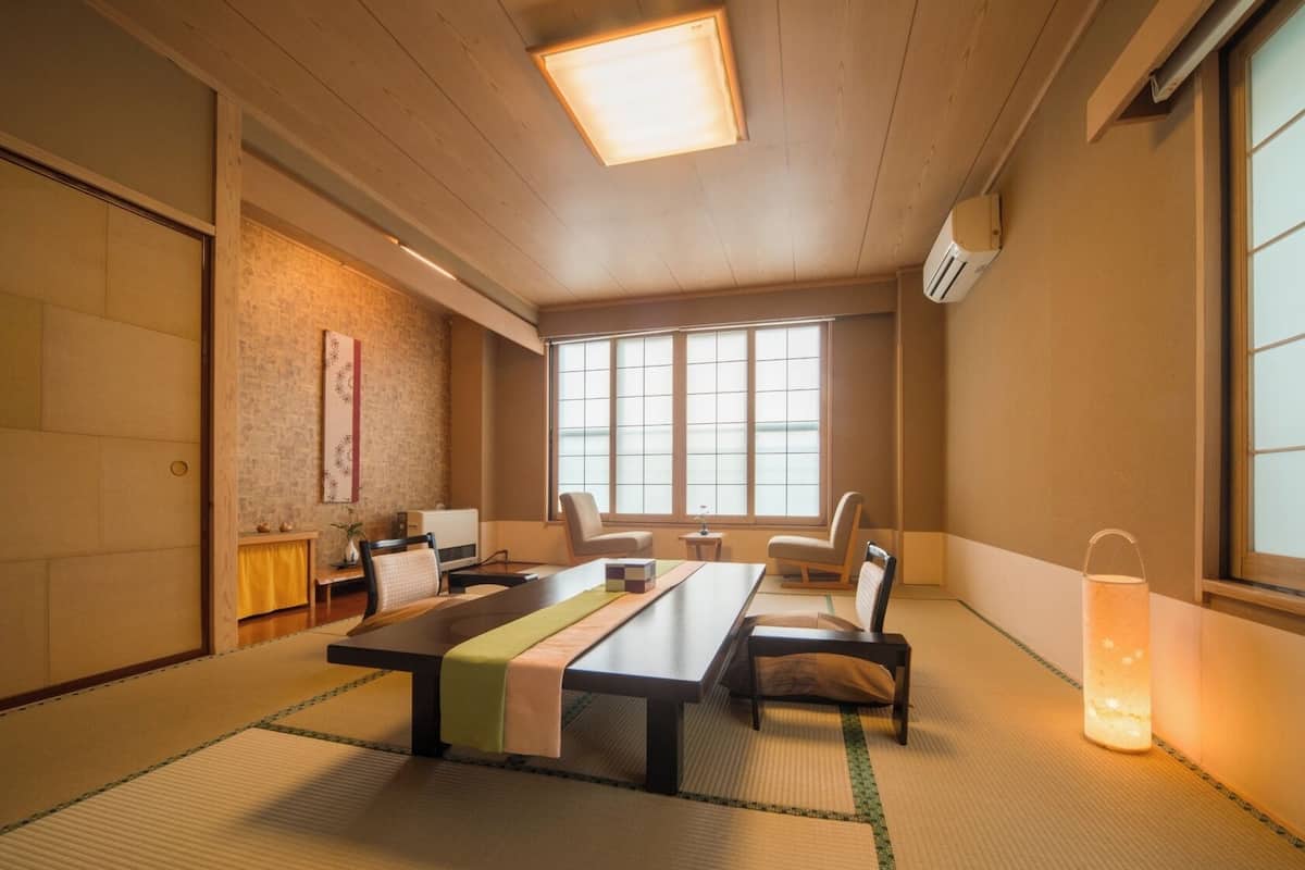 A traditional Japanese room with tatami flooring, a low table, chairs, a shoji screen, and a sliding door.