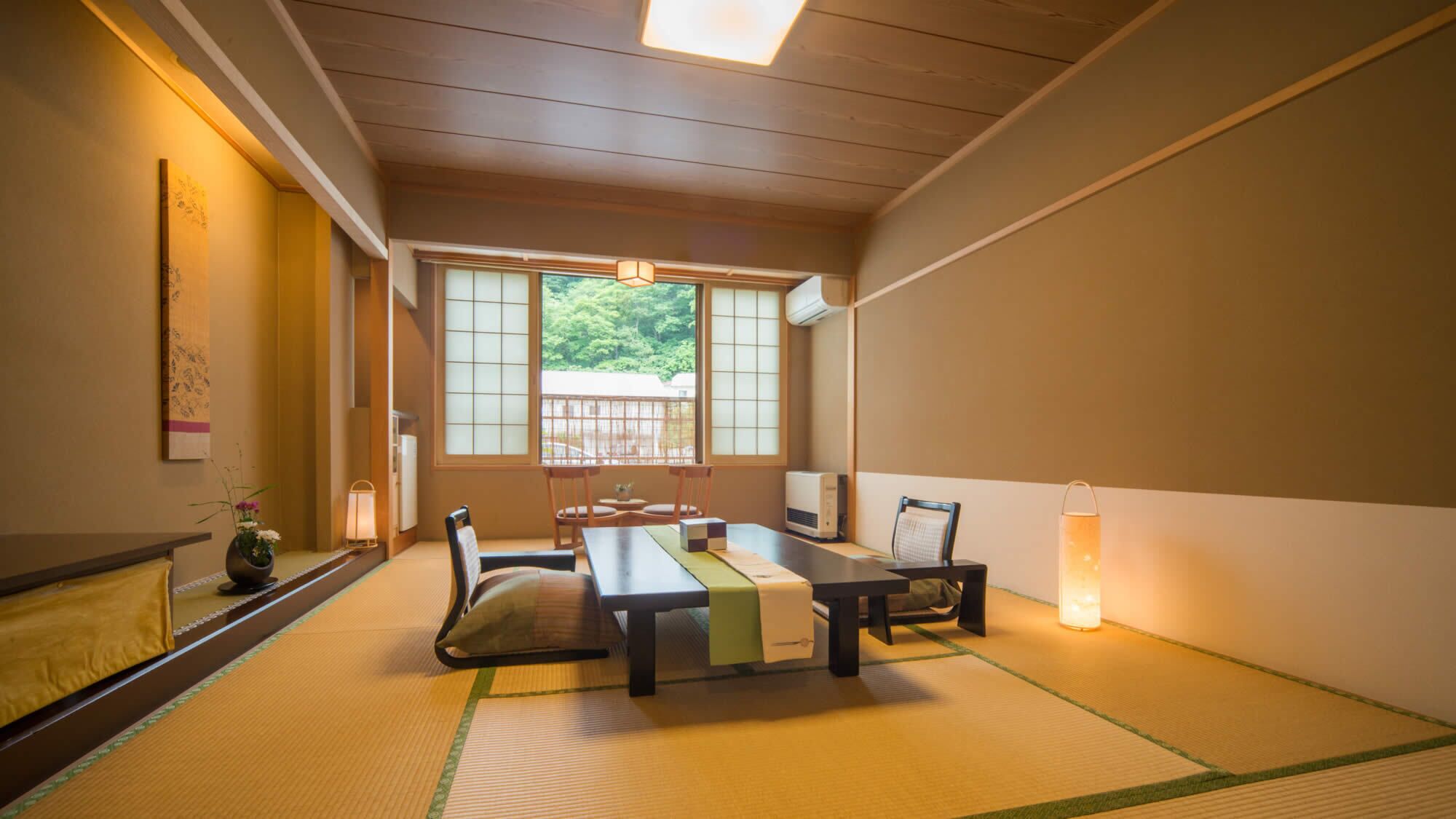 Una habitación japonesa tradicional con suelo de tatami, una mesa baja, sillas, un televisor y una ventana con vistas a zonas verdes.