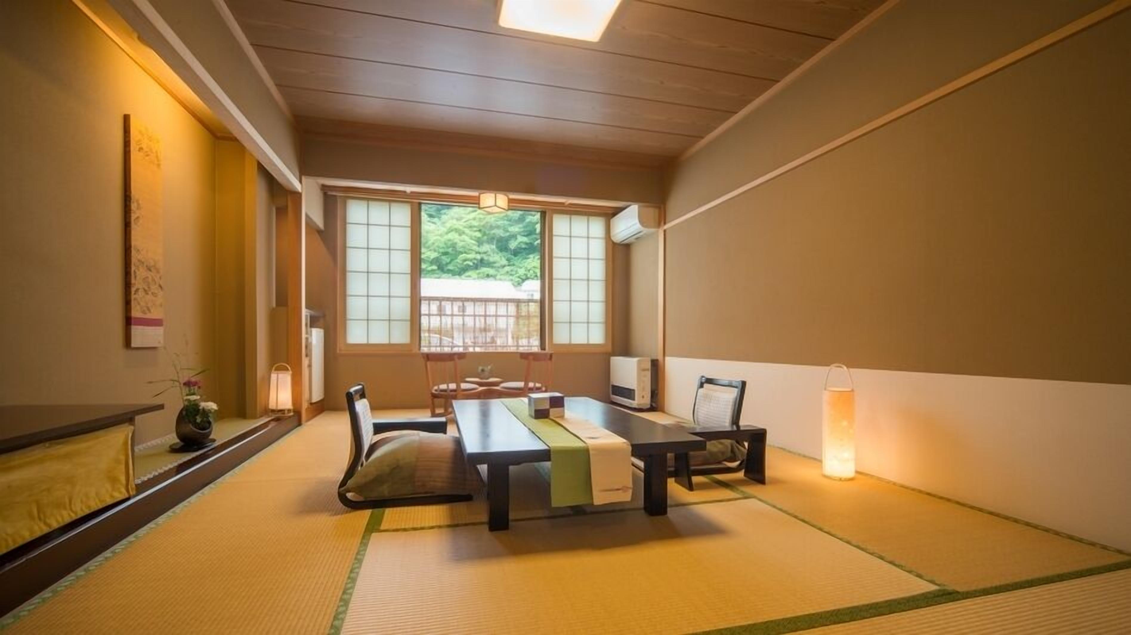 A traditional Japanese room with tatami flooring, a low table, chairs, a TV, and a heater.