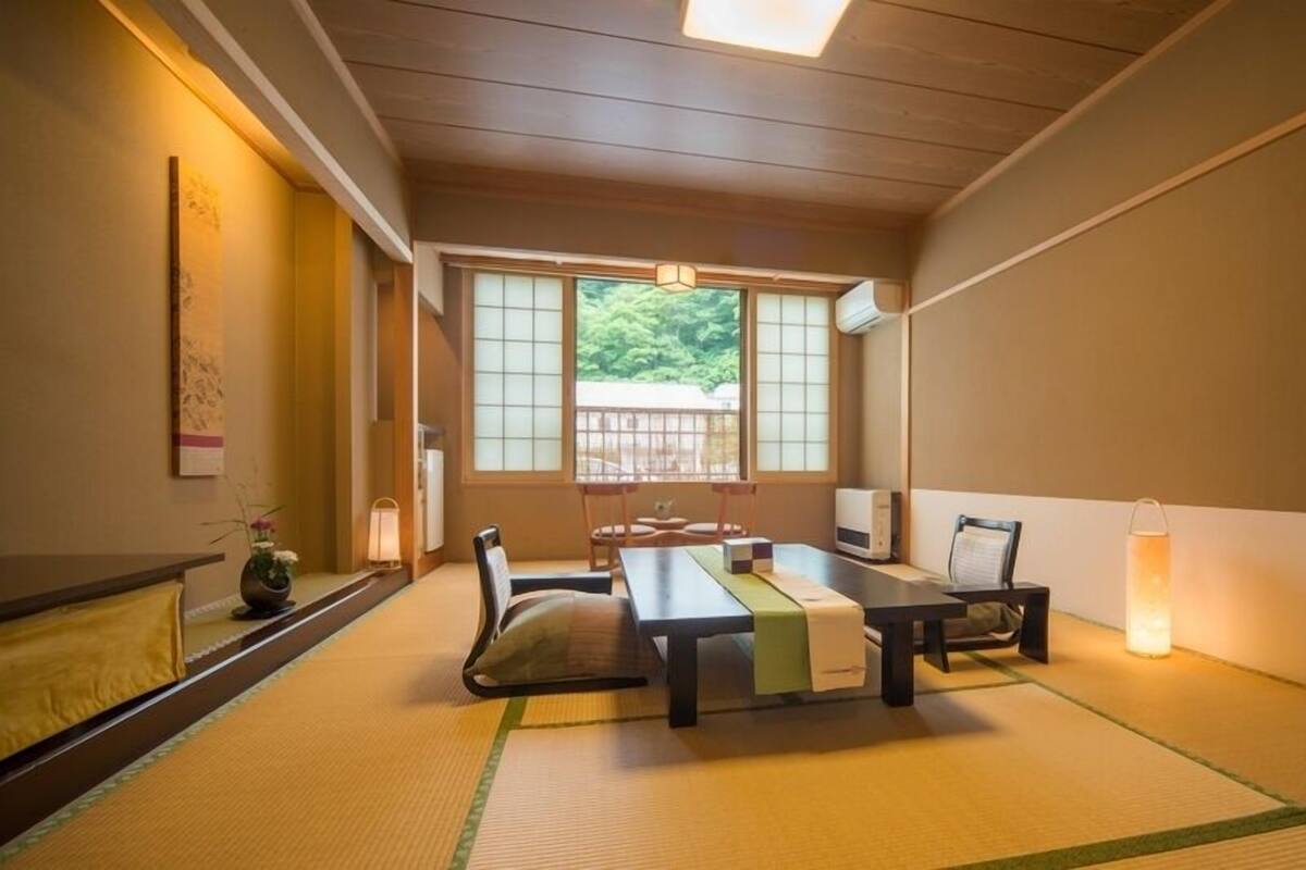 A traditional Japanese room with tatami flooring, a low table, chairs, a TV, and a heater.