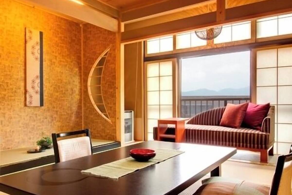 A traditional Japanese room with tatami flooring, a low table, a sofa with cushions, and a view through large windows.