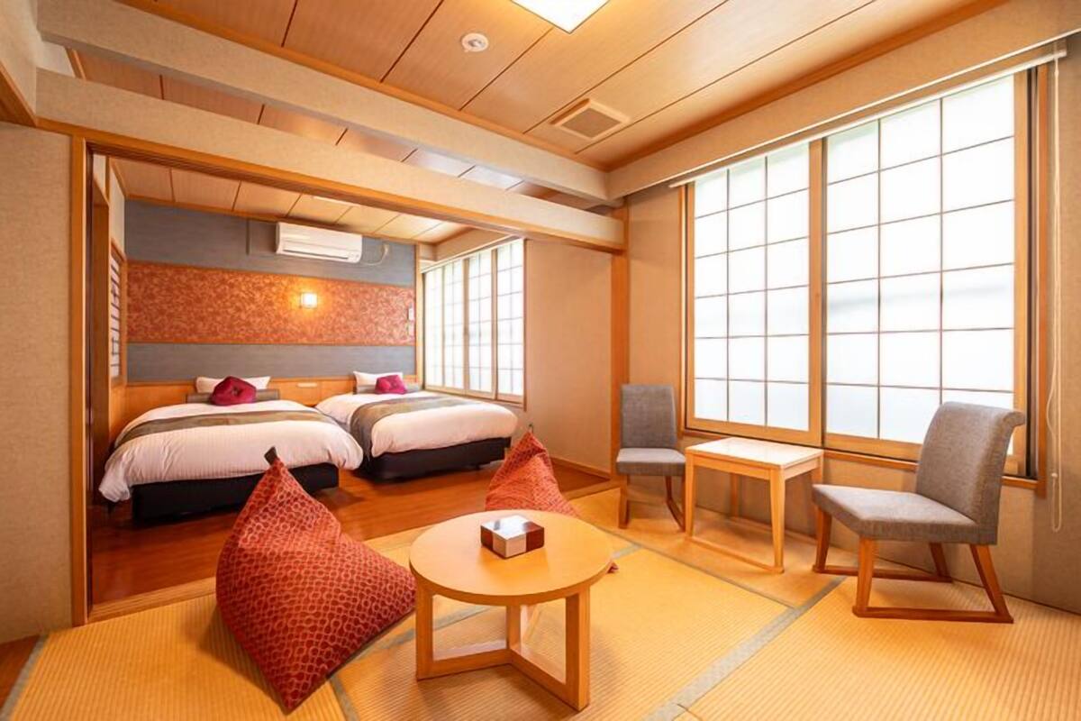 A traditional Japanese-style hotel room with tatami flooring, a futon bed, a small table, and a chair.