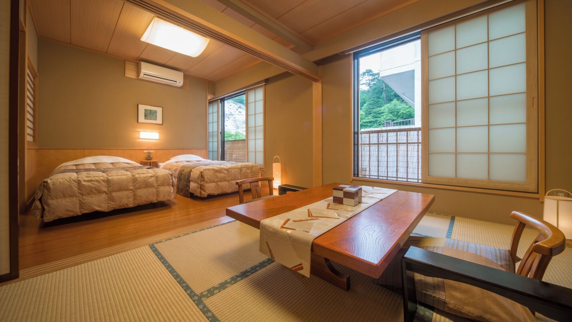 Una habitación japonesa tradicional con dos camas, una mesa de madera, esteras de tatami y grandes ventanales con vistas a la vegetación.