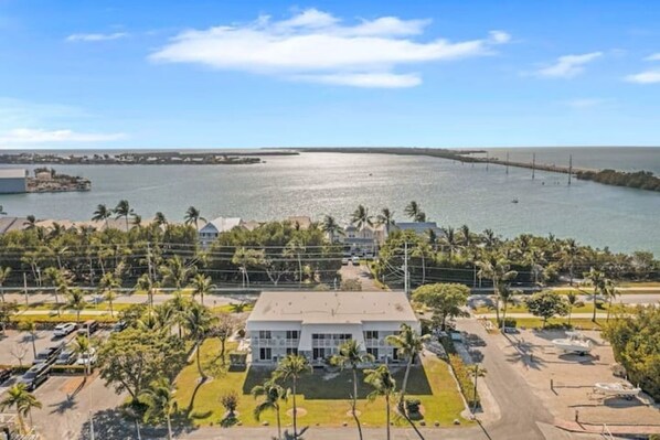 A coastal view with a white building, palm trees, and a bridge in the distance. - Oceanfront and Sunrise Views! (Marathon)