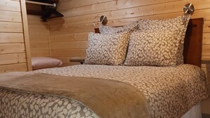 Un dormitorio tipo cabaña de madera con cama, almohadas y mesita de noche.
