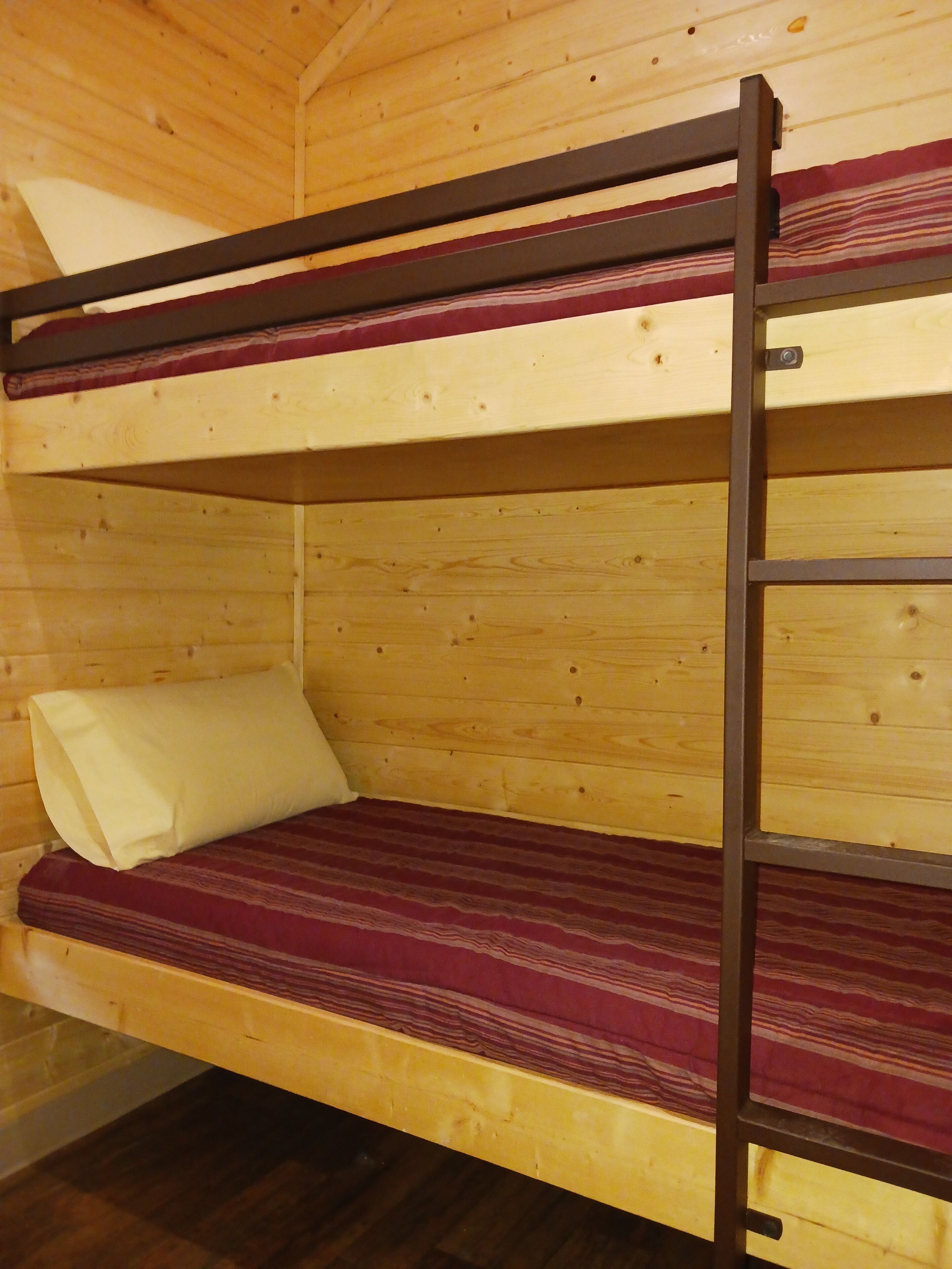 Una cama litera con estructura de madera y colchón a rayas rojas.