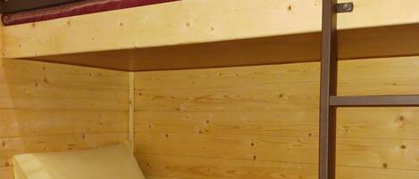 Una cama litera con estructura de madera y colchón a rayas rojas.