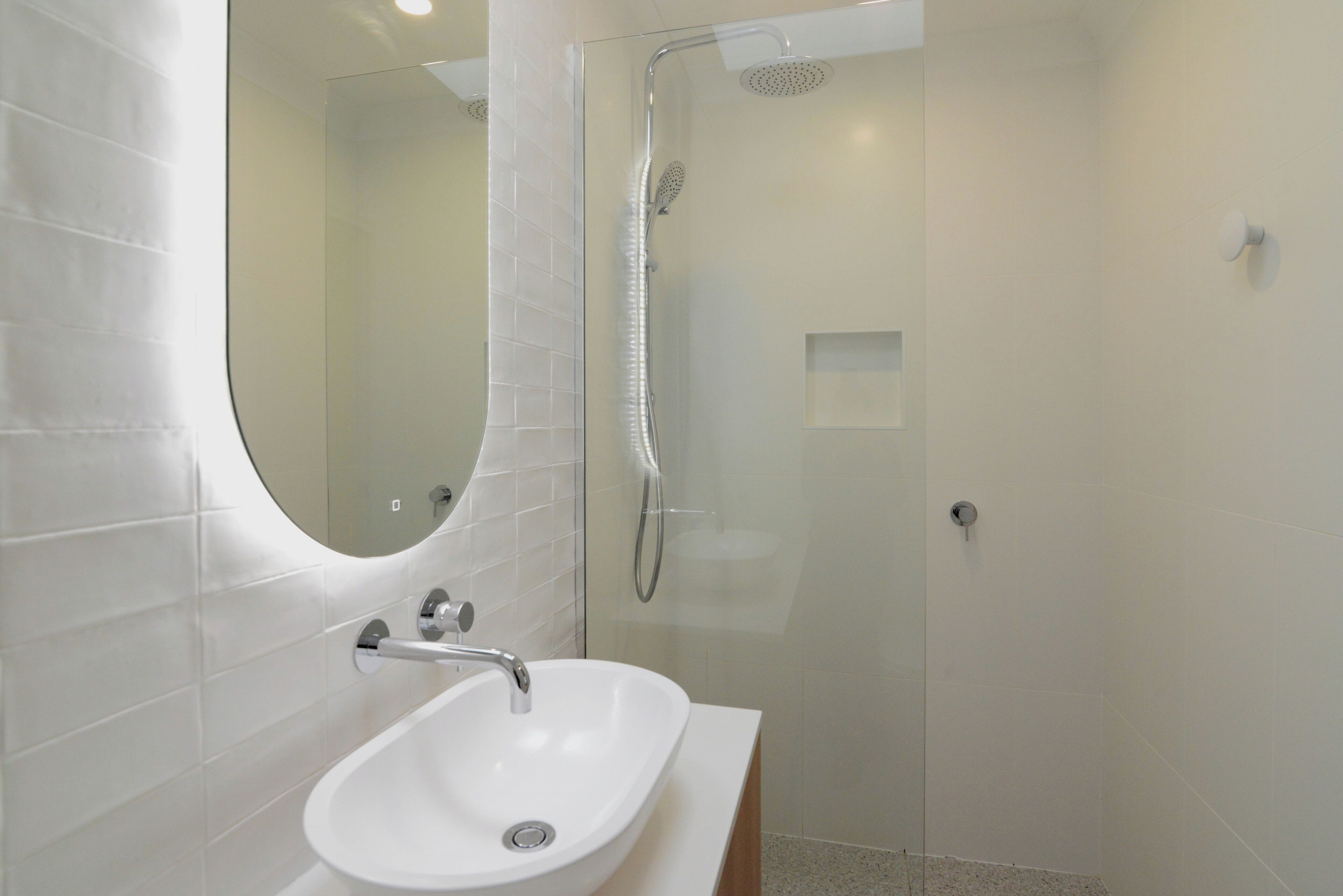 A modern bathroom with a white sink, a glass-enclosed shower, and a large mirror.