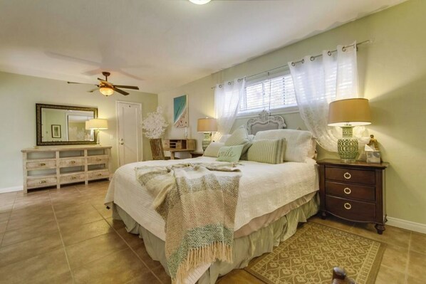 A bedroom with a bed, nightstands, a dresser, a ceiling fan, and a window with curtains.