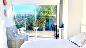 A bedroom with a large bed, a desk, and a chair. There is a sliding glass door leading to a balcony with a view of greenery. - Beach access main floor T3 apartment with amazing patio and plenty of space!  (Linguizzetta)