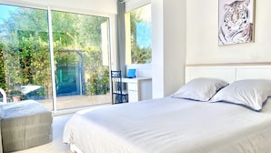 A bedroom with a large bed, a desk, and a chair, a sliding glass door leading to a garden. - Beach access main floor T3 apartment with amazing patio and plenty of space!  (Linguizzetta)