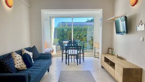 A modern living room with a dark blue sofa, a wooden TV stand, and a dining area with a table and chairs. - Beach access main floor T3 apartment with amazing patio and plenty of space!  (Linguizzetta)
