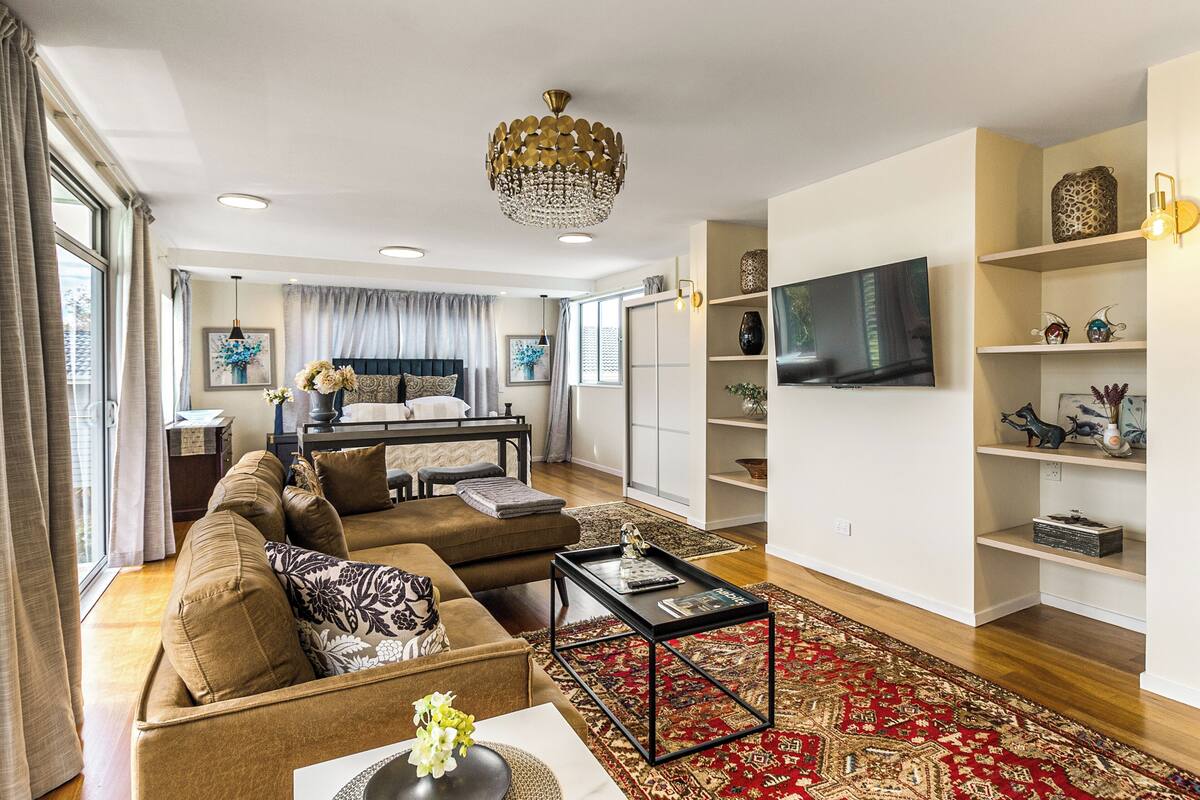 A modern living room with a sofa set, a coffee table, a chandelier, and a TV on the wall.