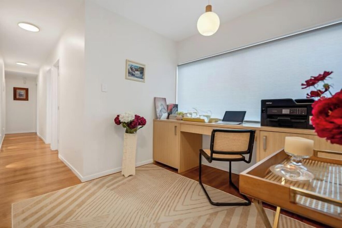 A hotel room with a desk, chair, and a dining table with a vase of flowers.