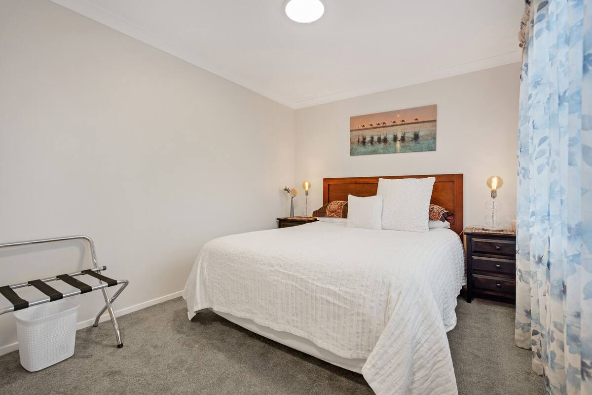 A neatly arranged bedroom with a large bed, a nightstand, a lamp, and a wall-mounted painting.