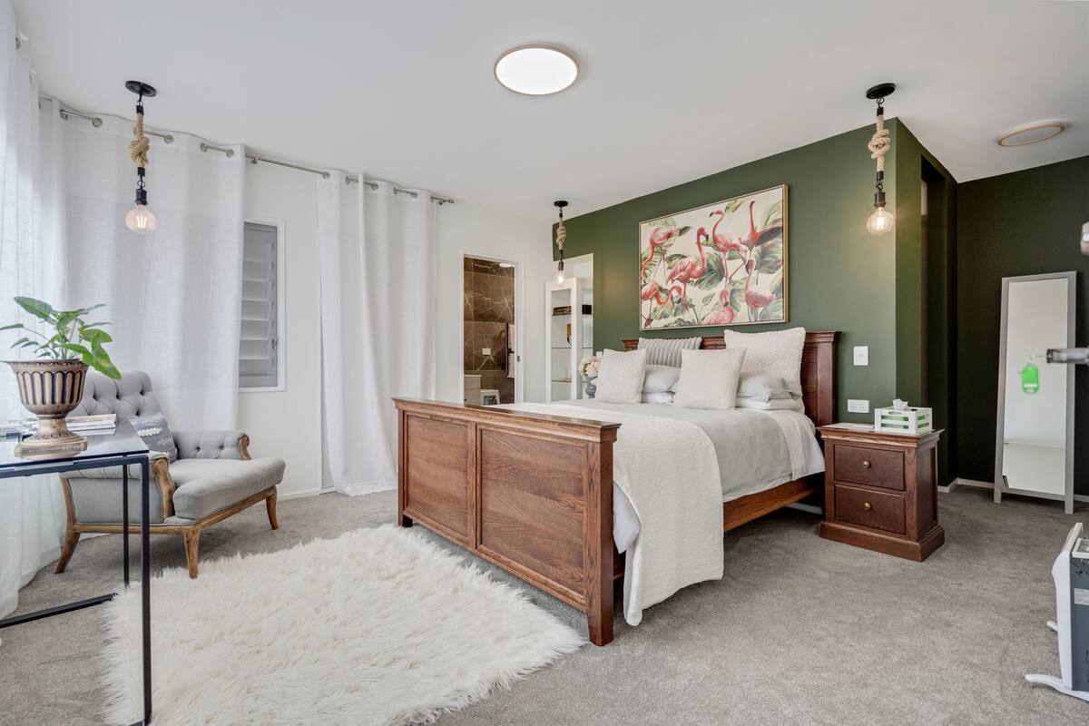 A bedroom with a large bed, a nightstand, a chair, a white furry rug, and a painting on the wall.