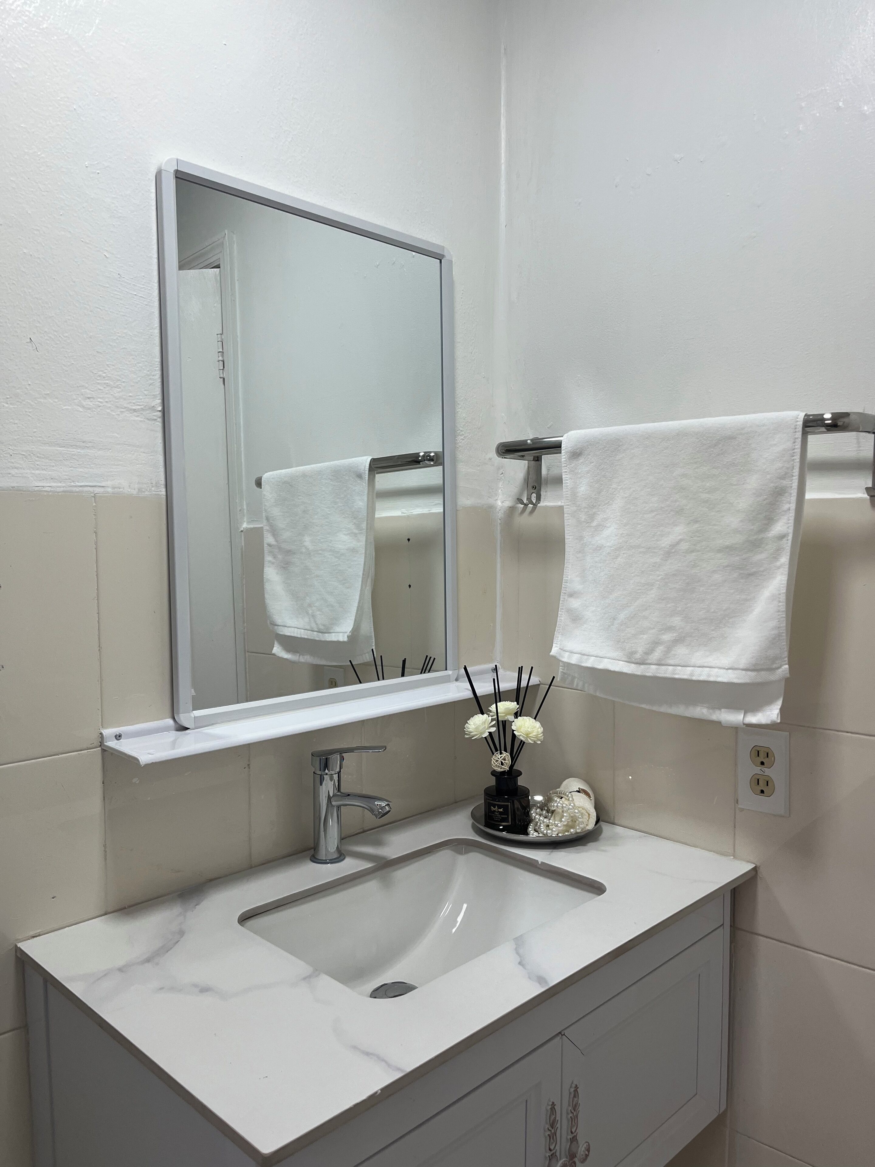 A bathroom with a white sink, a mirror, and two white towels hanging on towel bars.