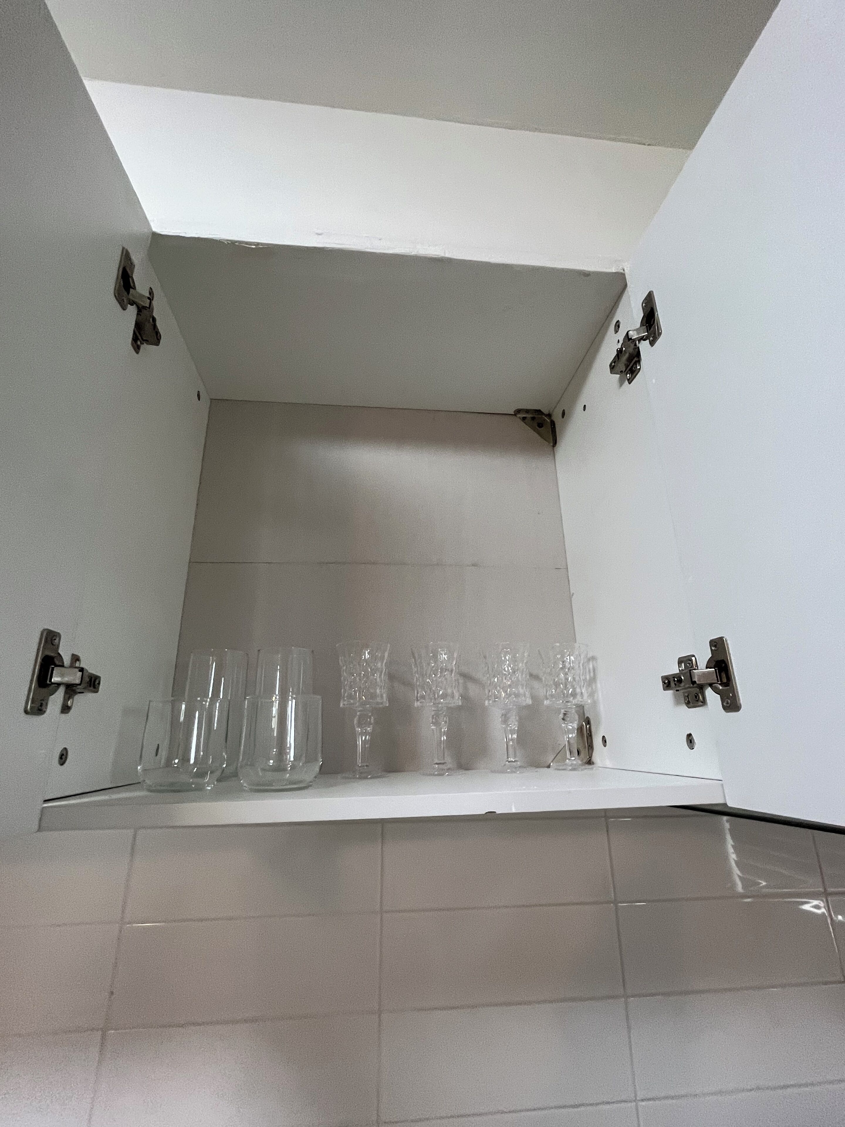 Un baño con piso de baldosas y una repisa con varios vasos transparentes.
