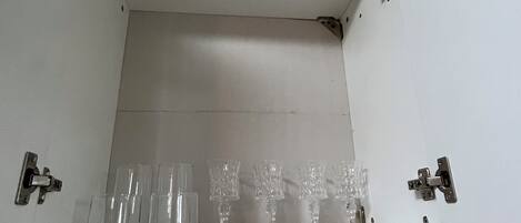 Un baño con piso de baldosas y una repisa con varios vasos transparentes.