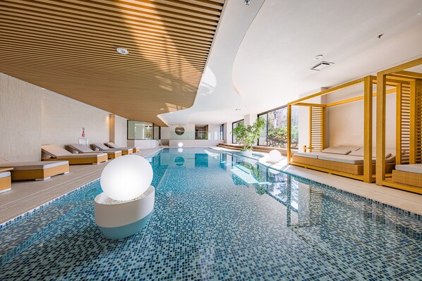 A modern indoor swimming pool with a tiled floor, lounge areas with seating, and a wooden ceiling. - nol hakone myojindai (Hakone)