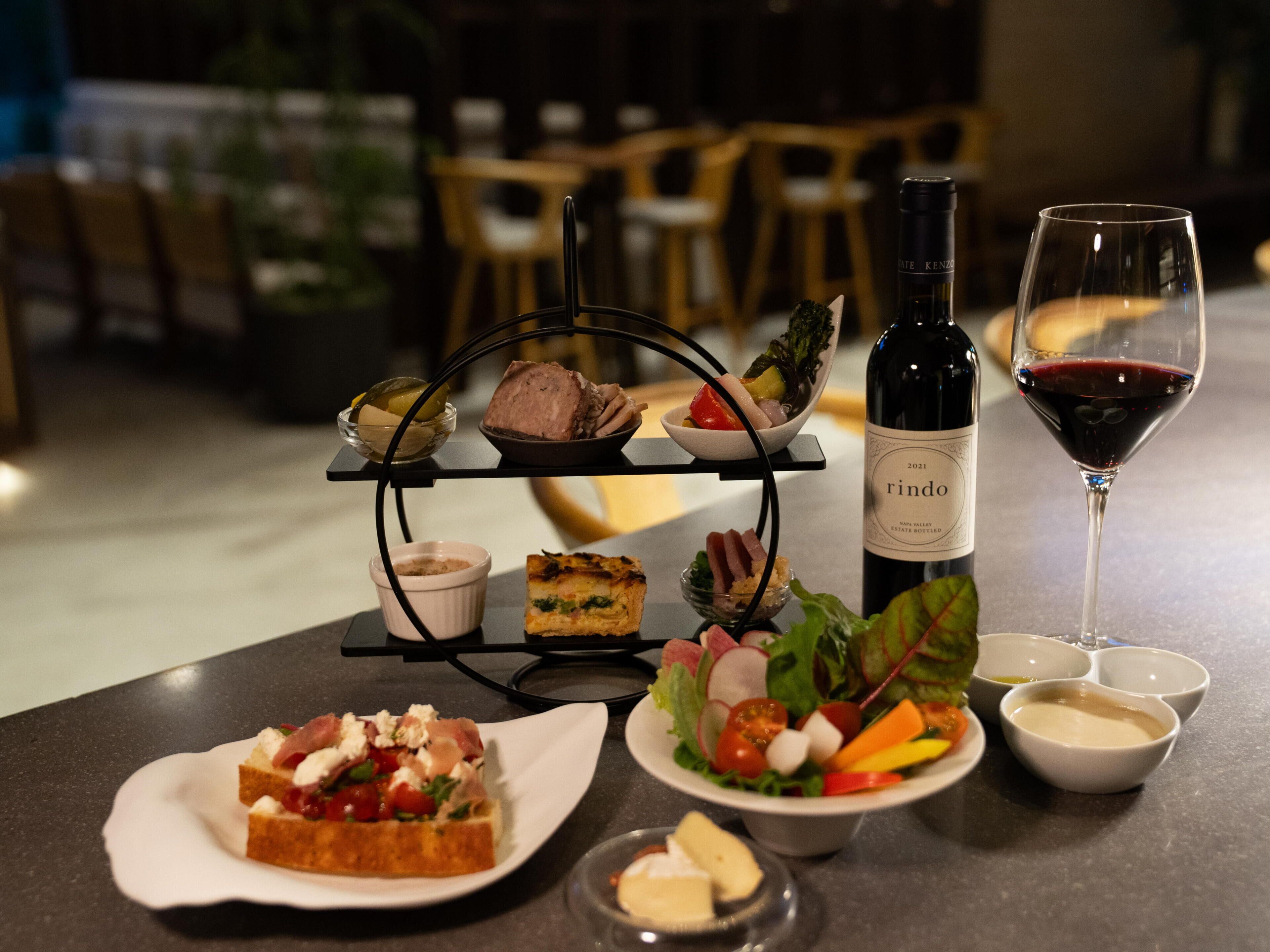 A dining table with a bottle of wine, a wine glass, and various dishes including a sandwich, salad, and a dessert.
