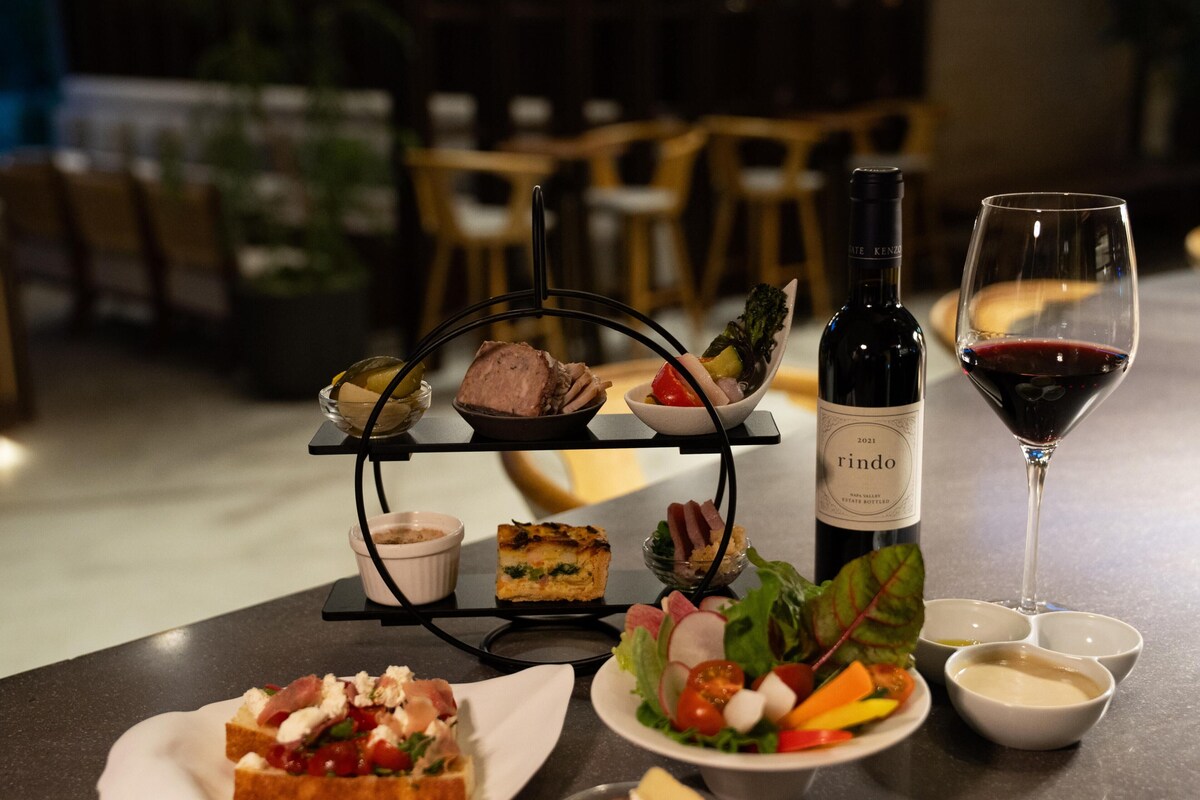 A dining table with a bottle of wine, a wine glass, and various dishes including a sandwich, salad, and a dessert.