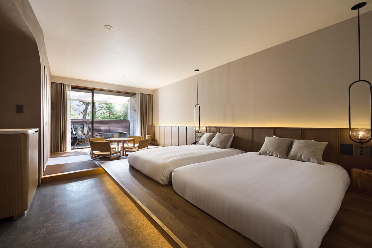 Quarto de hotel moderno com duas camas, um espaço de estar com mesa e cadeiras, e uma janela ampla com vista para o exterior.