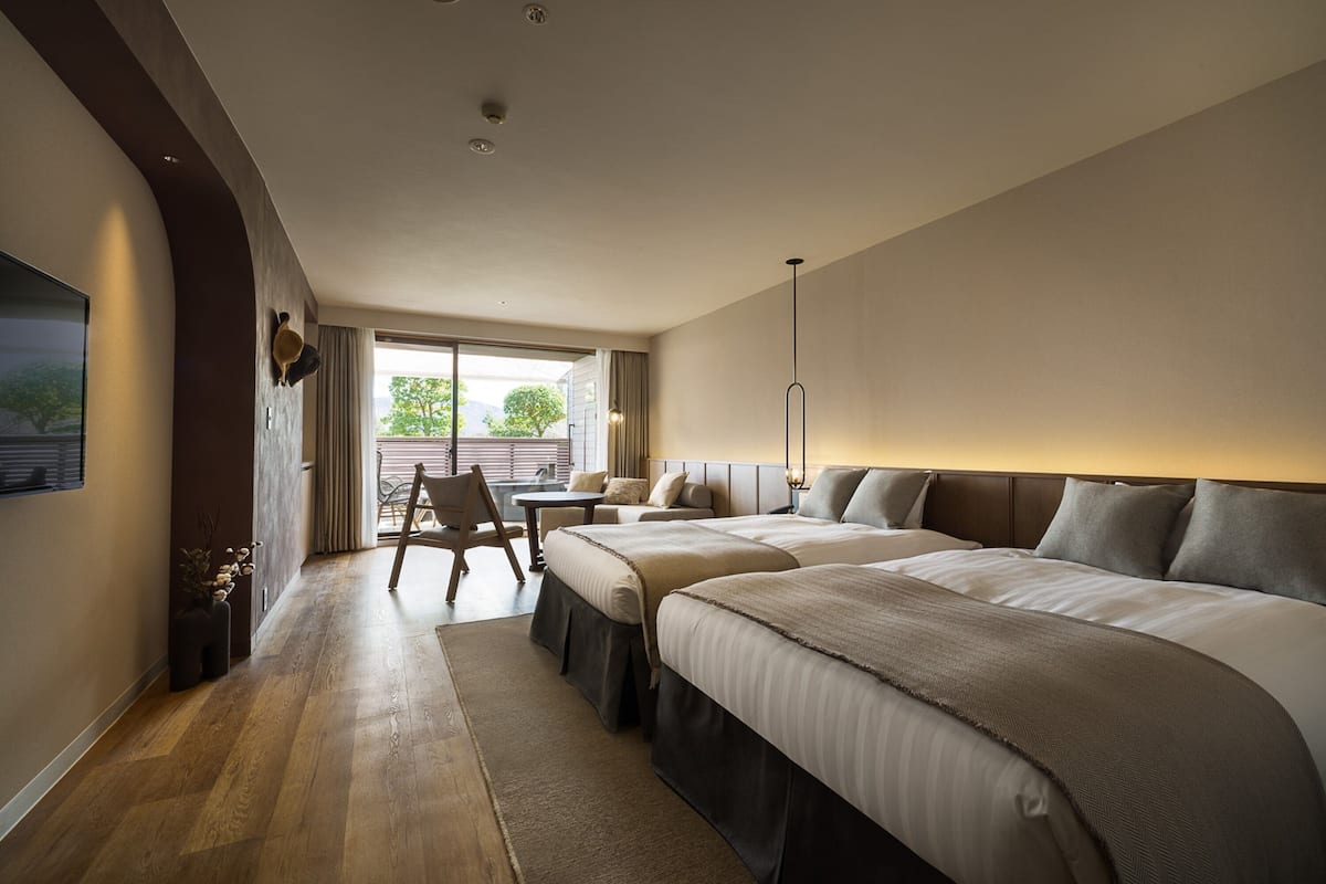 Quarto de hotel moderno com duas camas, uma escrivaninha e uma janela ampla com vista para o exterior.