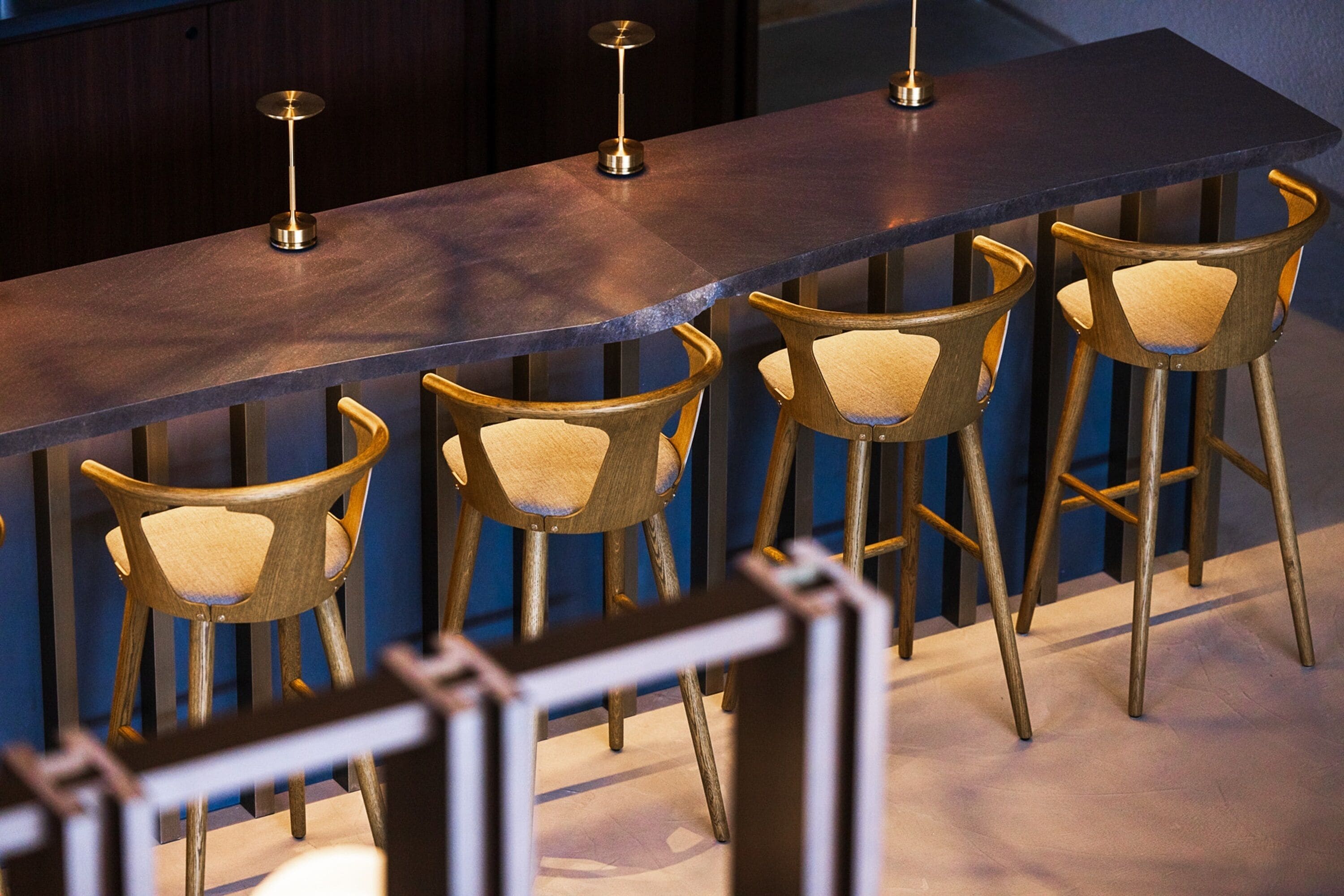 A bar area with a long counter and four wooden bar stools with cushioned seats.