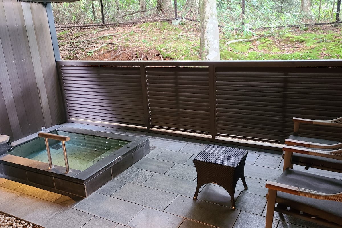 Uma área de spa com hidromassagem, duas cadeiras de vime e vista para uma área arborizada.