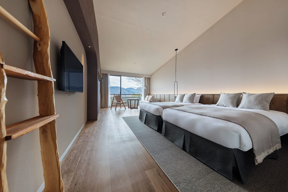 Quarto de hotel moderno com uma cama grande, uma mesa e uma televisão presa na parede.