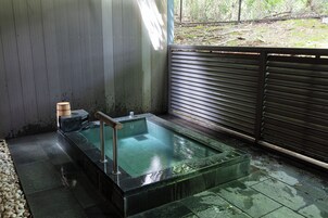 Un área de spa con un jacuzzi envuelto en vidrio, escalones de piedra y una valla de madera.