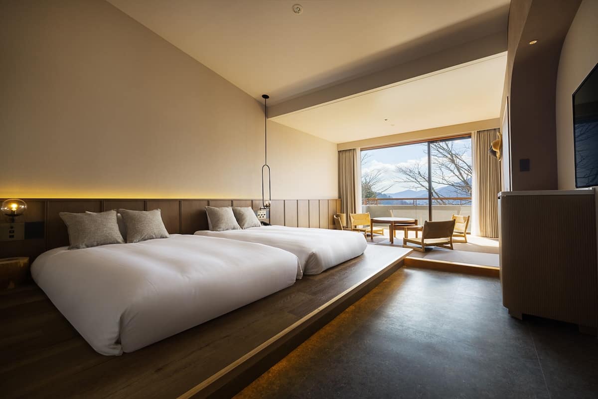 Quarto de hotel moderno com duas camas grandes, área de refeições e vista para montanhas.