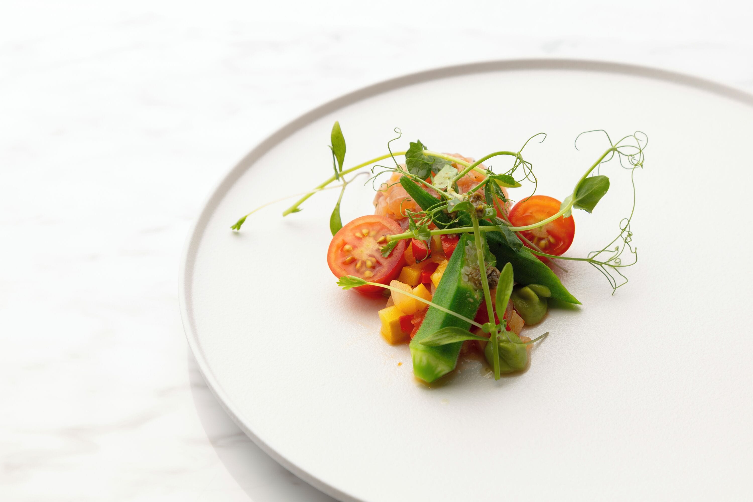 A white plate with a salad of tomatoes, greens, and yellow cubes.